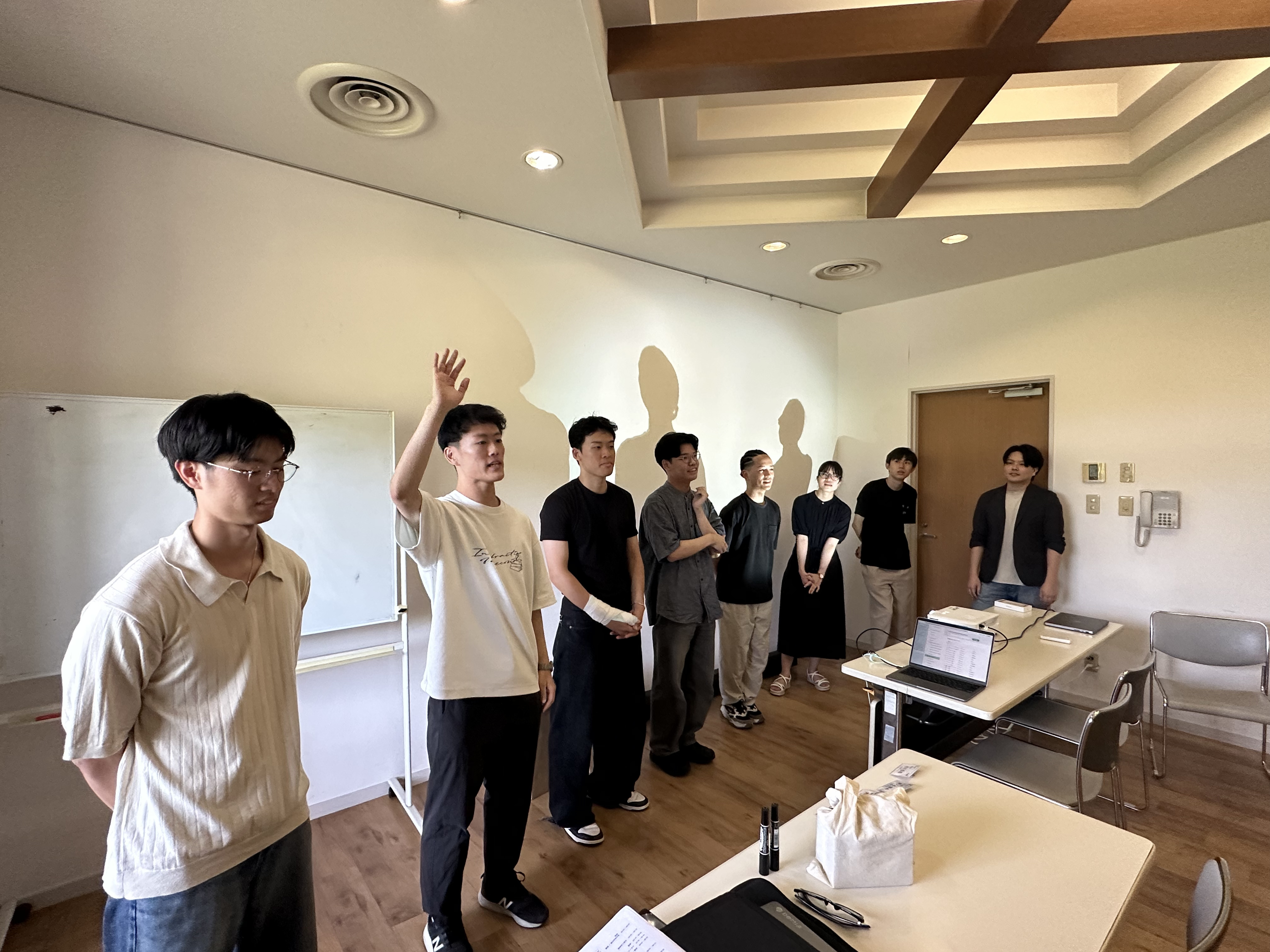 開講式で横一列に並び、手を挙げて自己紹介する講師・スタッフ