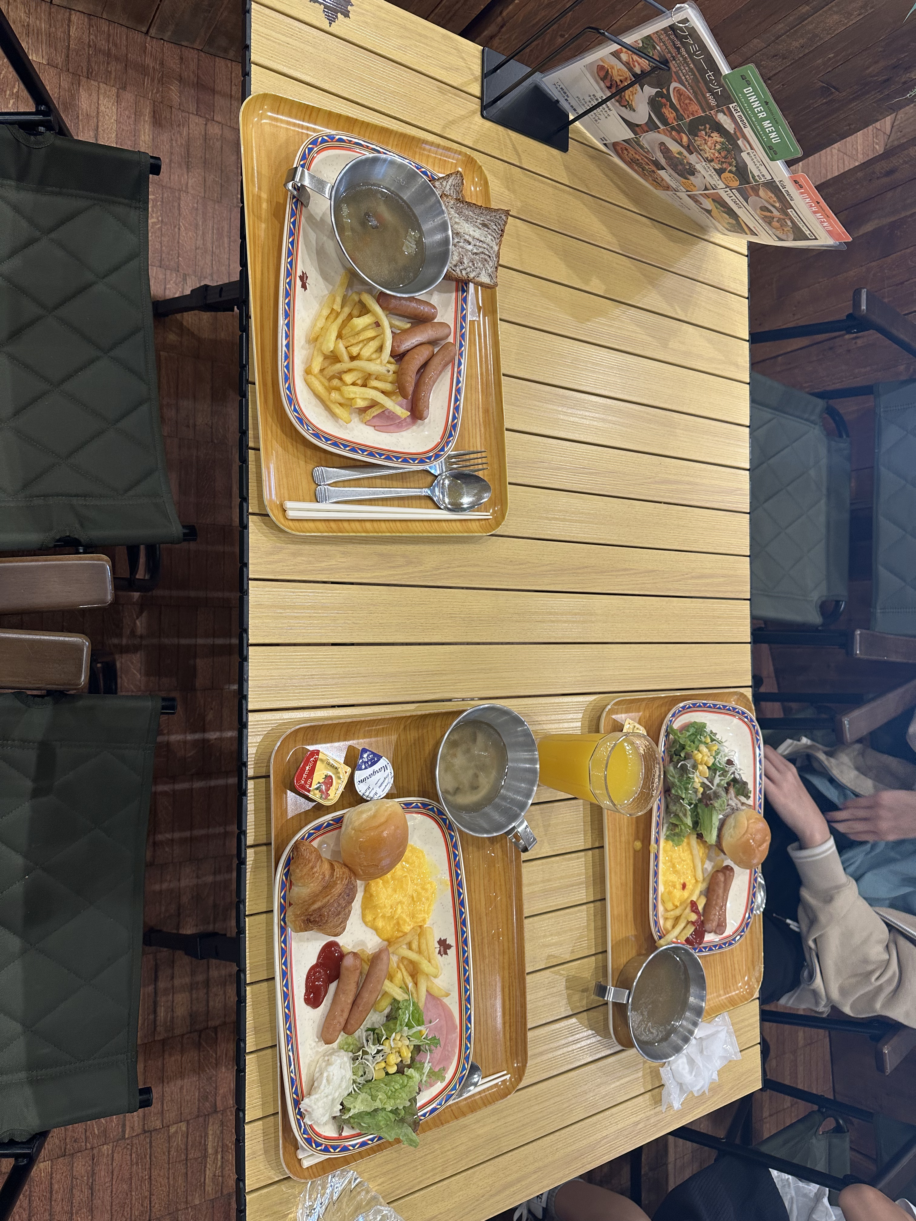 テーブルに並んだ朝食のトレイ（スクランブルエッグ、ソーセージ、パン、スープなど）