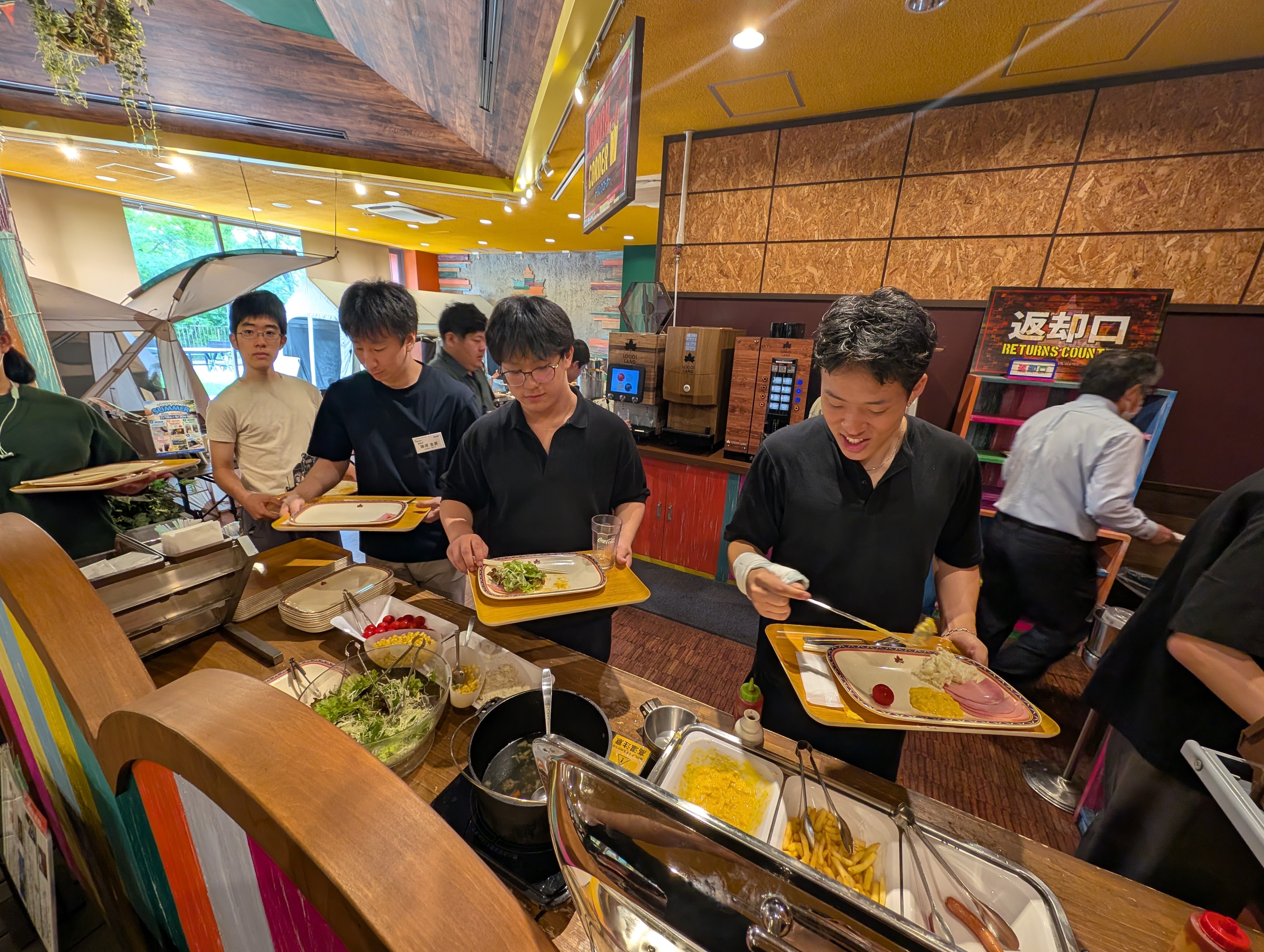バイキング形式の朝食会場で、トレイを持って料理を取り分ける生徒とスタッフ