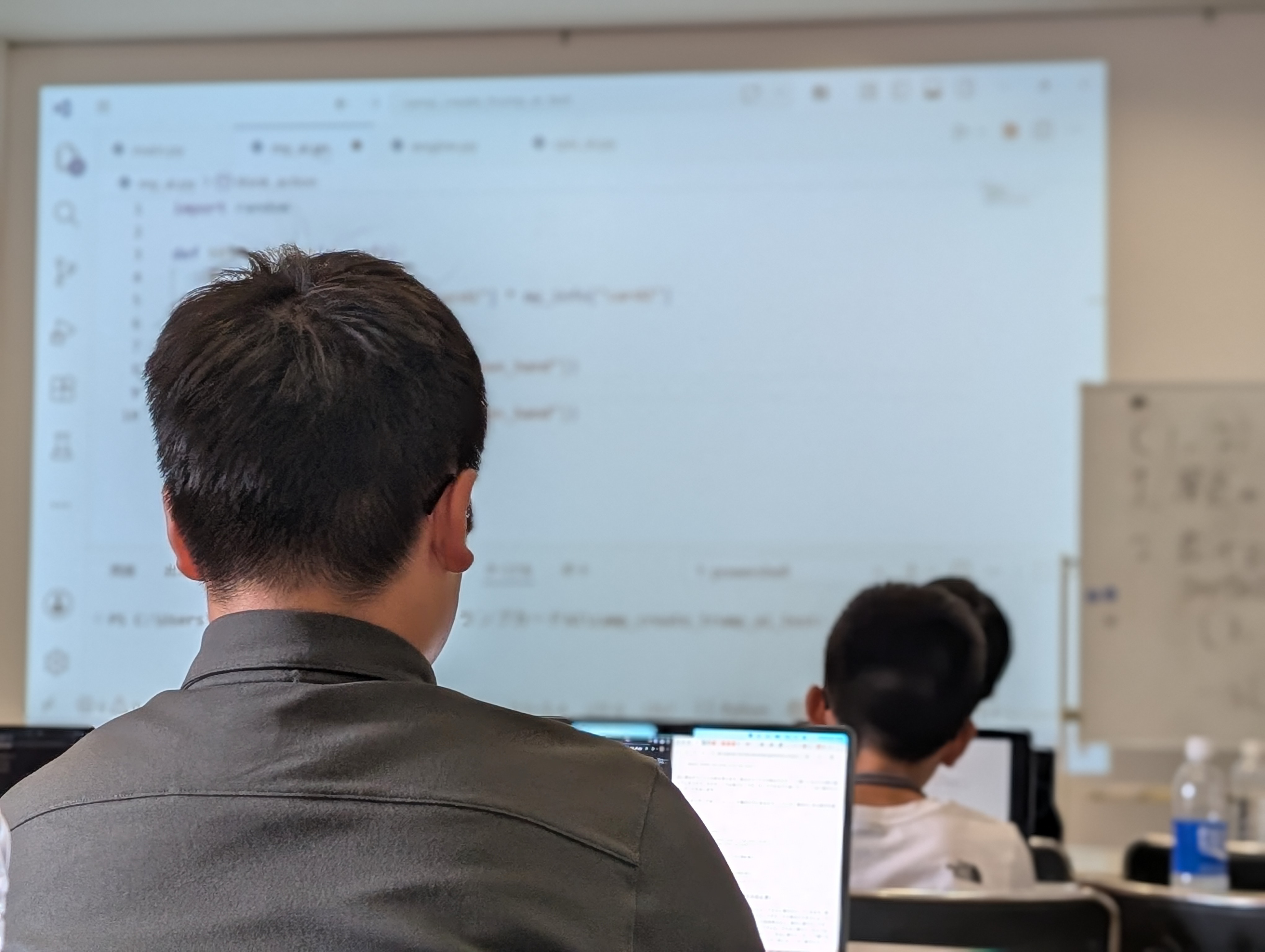 前方のコード画面を見ながらプログラミングに取り組む生徒