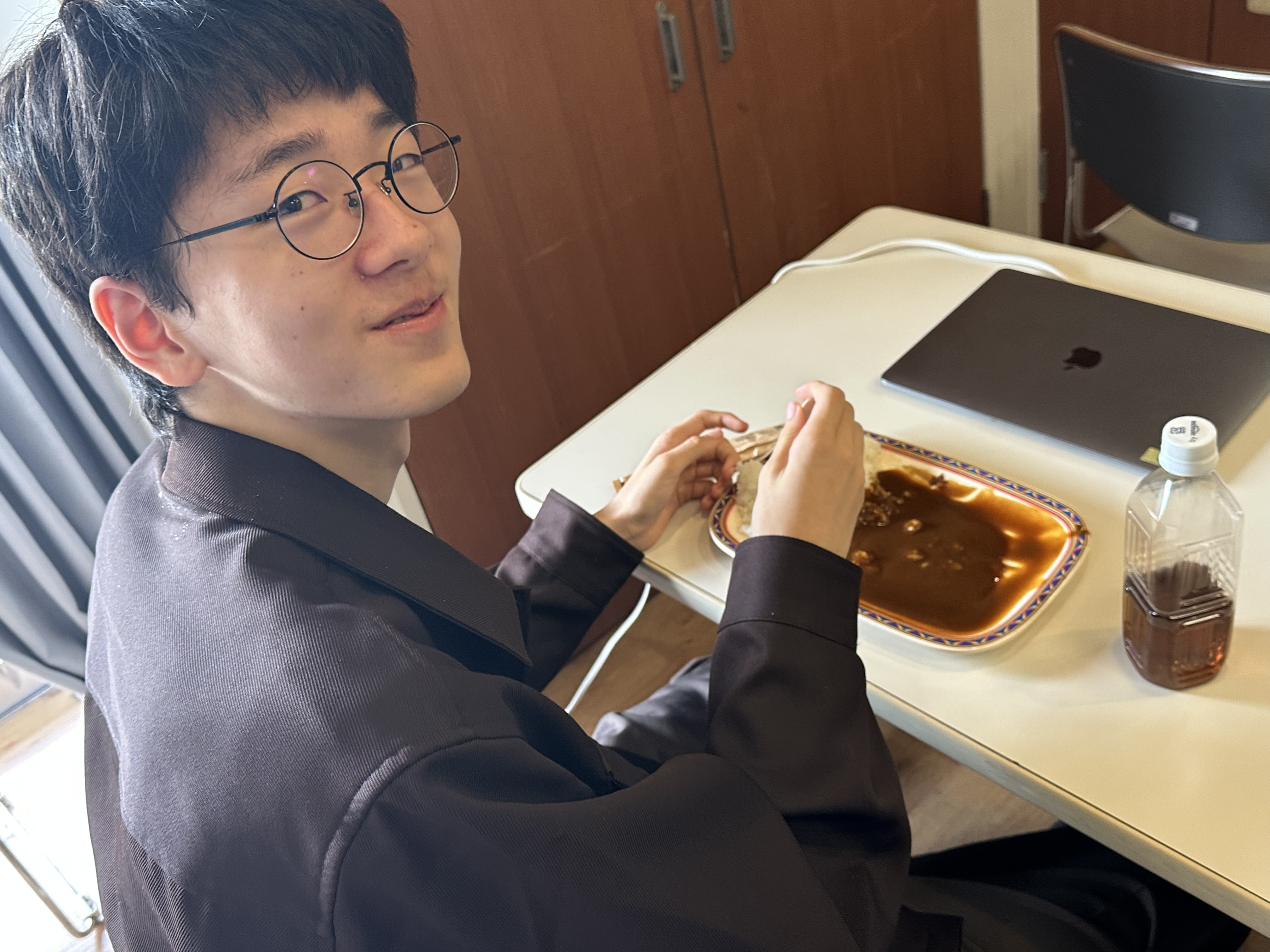 ノートPCを置いた机で、昼食のカレーライスを食べる生徒