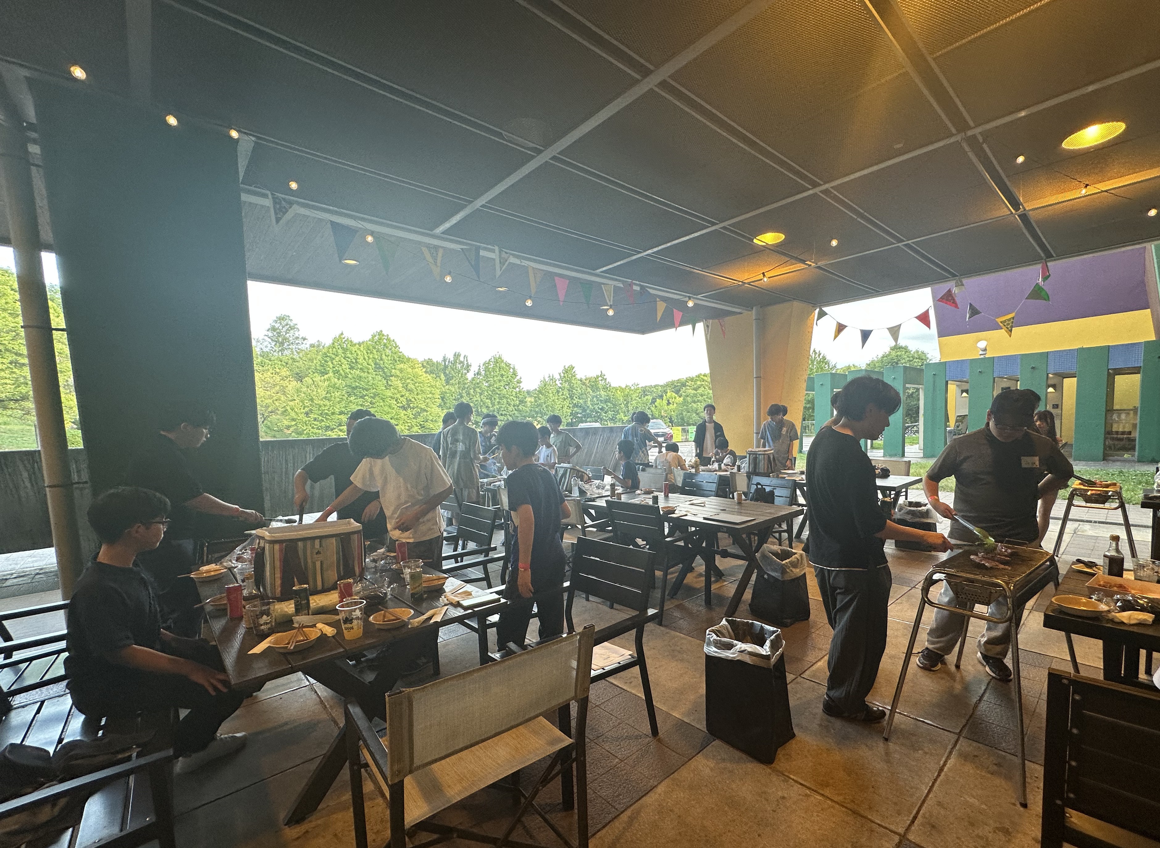 ガーランドが飾られた屋根付きのBBQ会場で、コンロを囲む生徒とスタッフ