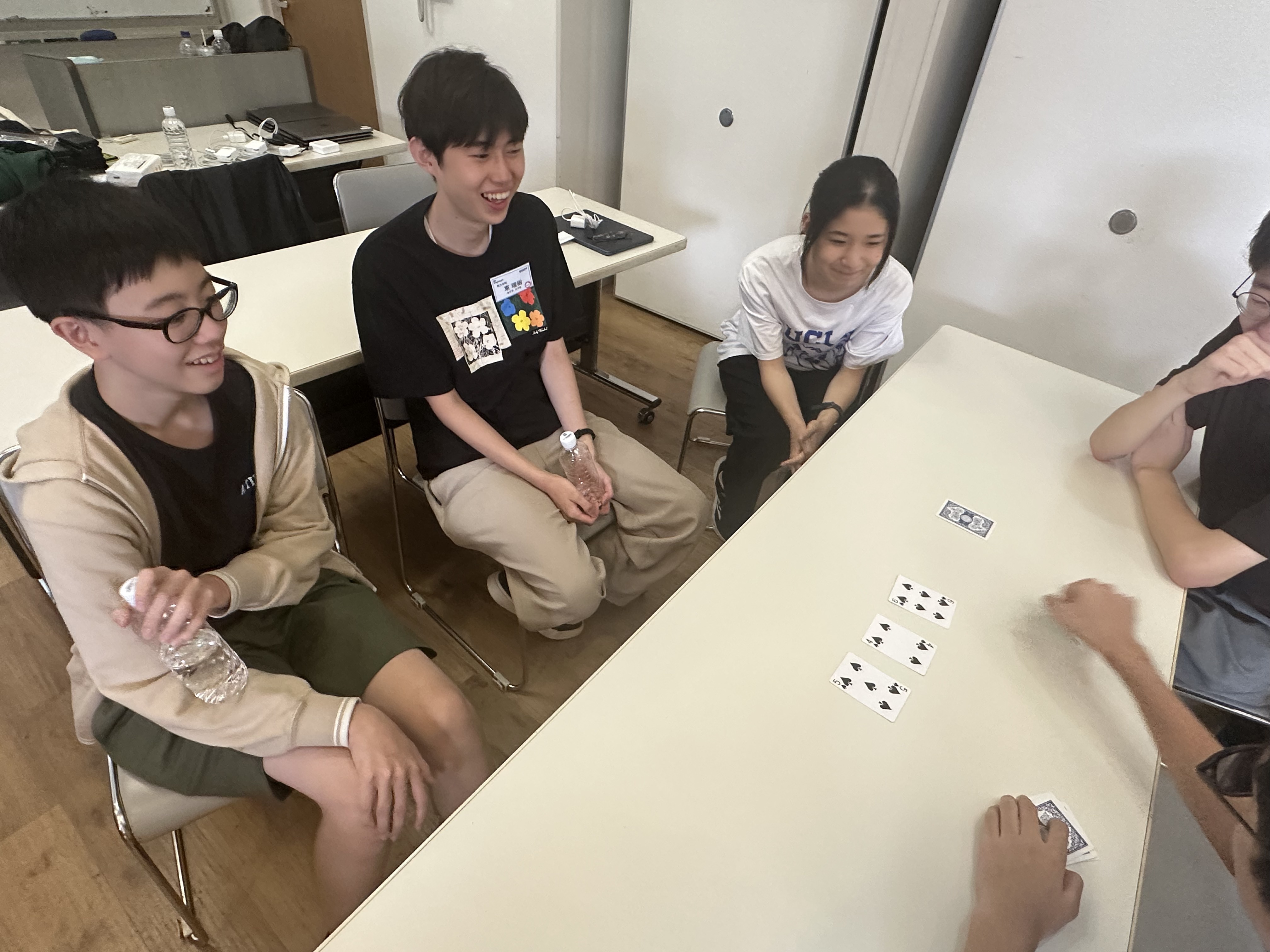 テーブルにトランプを広げ、ボードゲームitoに取り組む生徒とスタッフ
